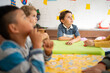 © Alan - Preschool children sitting around a table listening attentively, with one boy looking up in deep thought. Kindergarten learning environment focused on attention, curiosity, and early education