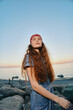 © SHOTPRIME STUDIO - young woman with long curly hair wearing a red bandana and denim outfit enjoying sunset at rocky beach with calm sea and clear sky in warm evening light