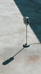 Fototapete - Classic Vintage Microphone Standing Tall on Minimalist Concrete Surface with Dramatic Shadow for Podcast and Professional Audio Branding