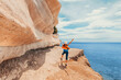 © EdNurg - Female hiker with open arms enjoying the beautiful seascape and the sedimentary rocks in a sunny day