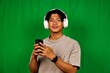 © Sesat_pictures - Young Man Wearing Large White Headphones Holding Smartphone in Front of Green Screen