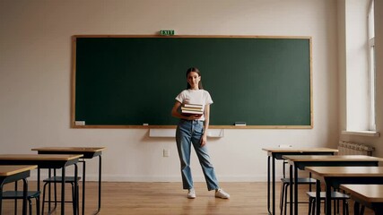 Aufkleber - Confident student stands in an empty classroom, holding books, ready for the academic year, against a backdrop of a chalkboard and organized desks