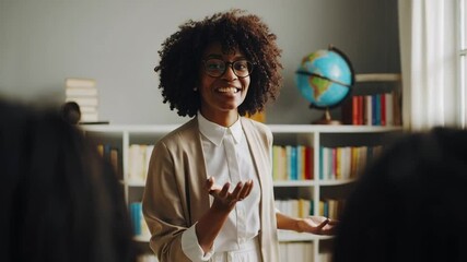 Poster - Professional educator wearing glasses and light brown jacket engaging students during dynamic classroom discussion, gesturing expressively near bookshelf with globe