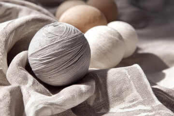 Aufkleber - Soft gray wool ball resting on natural linen fabric, surrounded by neutral colored yarn balls, creating minimal and cozy atmosphere with gentle sunlight