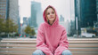 © hdesert - Casual young woman wearing a pink hoodie, sitting on a city bench, relaxed urban vibe