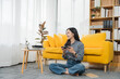 © Wicitr - Woman playing video games at home: A young woman smiles happily as she sits cross-legged on the floor of her living room, engrossed in playing a video game on her mobile device.