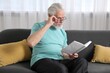 © New Africa - Senior man with vision problem reading book on sofa at home