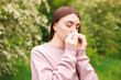© New Africa - Woman with paper tissue suffering from seasonal pollen allergy near blossoming shrub on spring day