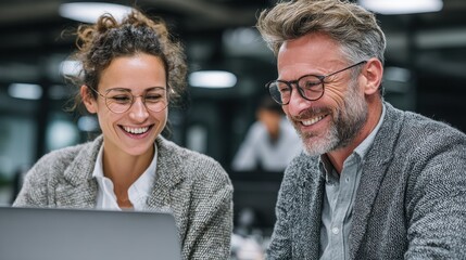 Poster - Two employees smiling while collaborating on a project at a laptop during the workday at the office