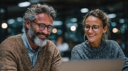 Poster - Two employees smiling while collaborating on a project at a laptop during the workday at the office