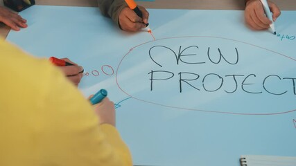 Poster - A group of people engages in a brainstorming session for a new project, using colorful markers on blue paper. This creative workspace fosters collaboration and innovation. SACTR