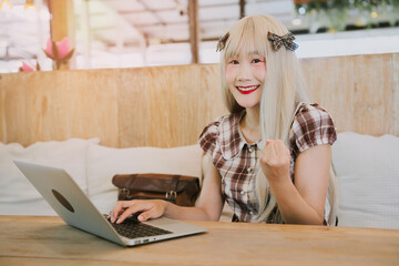 Poster - Young Asian woman with long hair smiles and works on laptop in cozy cafe setting with natural light and warm ambiance
