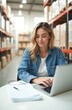 © Vadym - Young female entrepreneur works at warehouse office. Woman uses laptop, organizes delivery, shipping, logistic process. Business owner managing online store, small business. E-commerce retail.