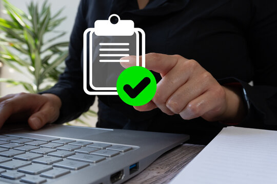 Businesswoman in front of a laptop pointing at a virtual icon of a clipboard with a check mark