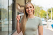 © luismolinero - Young blonde woman holding a credit card at outdoors smiling a lot