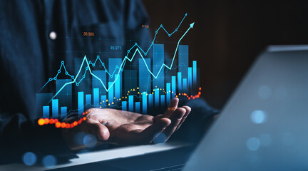 Poster - Businessman holding holographic financial chart with upward growth lines and bar graphs above hands in dark office environment, symbolizing analytics concept.