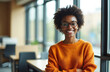 © Pete - Smiling African woman with glasses, braids wearing orange sweater in office setting. Looking at camera with arms crossed, conveying professionalism, confidence. Suitable for business, education,