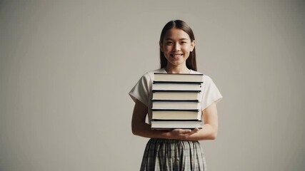 Aufkleber - Young female student smiling brightly while carrying stack of books, standing against white background and preparing for academic learning journey