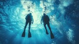 Two scuba divers ascending in the ocean. Sunlight streams down through the water