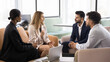 © fizkes - Strategic conversation in creative space. Busy multicultural entrepreneurs sit close together on sofas discuss project plan collaborate on innovative startup brainstorm ideas on casual team meeting