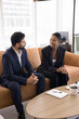 © fizkes - Comfortable collaboration. Vertical shot two business professionals coworkers of diverse gender ethnicity have casual conversation sitting on sofa taking break from working on documents chat drink tea