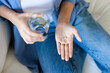 © Dorde - Woman's Hands Holding Blue Pill With Glass Of Water While Sitting On Couch In Living Room