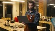 © Yuliia - Caucasian wood master man typing laptop shopping app online in workshop builder handyman guy using Internet pc carpenter male buying goods artist architect browsing website small business cyberspace