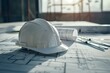 © juliars - White hardhat is lying on construction plans on a table, tools are spread around it