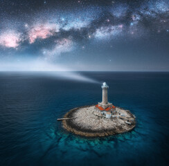 Wall Mural - aerial view of lighthouse on smal island in the sea and milky way at night in summer. beautiful ligh