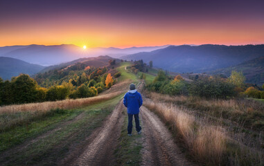 Wall Mural - man on the rural gravel road on the hill looking on mountains in fog at colorful sunrise in autumn i