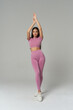 © Dmitry Tsvetkov - Woman in pink athletic wear strikes a graceful pose, with arms raised above head, on a minimalistic background. She wears white sneakers, exuding elegance and fitness