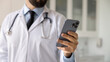 © fizkes - Close up banner shot of smartphone in hand of male doctor. Medical practitioner, healthcare professional man chatting with patient on cellphone, giving online support, remote consultation