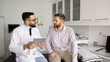 © fizkes - Young medical physician meeting with male patient in hospital examination room, talking to man, holding tablet for making records, filling electronic survey, explaining examination results