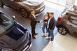 © Anastasiya - Dealer shaking hands with young couple in car showroom from aerial view. Symbolic moment of trust and closure in vehicle purchase decision, above shot