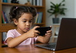 © Pixel Studio - Young girl playing games on smartphone near laptop at home learning technology and digital literacy