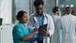 © Yuliia - Doctors cooperation teamwork Indian Arabian woman nurse therapist asking advice African American man doctor doc pediatrician therapist practitioner discussing holding digital tablet device at clinic