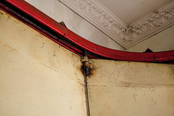 Poster - Abstract view showcases a damaged corner, featuring a red painted metal frame, aged walls with staining, and an ornate ceiling. The scene evokes decay and an antiquated aesthetic.