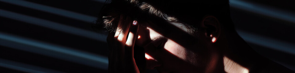 Poster - Close-up of a Person's Face Partially Obscured by Shadow and Hand, with Light and Blinds in Background