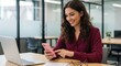 © MstMorjina - Photo of young woman smiling while using phone at office desk