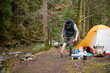 © Василь Івасюк - Hiker man with injured leg using first aid kit near the tent in the forest. A stressed trekker complaining alone in the mountain with broken knee. Traveler bandages leg after injury