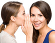 © TransPicHub - Two women, one whispering a secret to the other, who smiles brightly against a black background.
