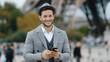 © pvl0707 - Young man in a hat smiles while using a mobile phone near the Eiffel Tower in Paris, showcasing the joy of travel against a famous landmark backdrop