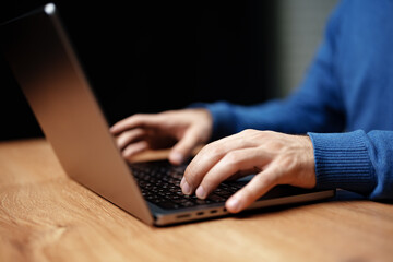 Poster - Hands typing on a laptop on a wooden table with a focus on the workspace atmosphere
