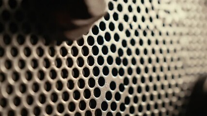 Close Up Metal Mesh with Evenly Spaced Holes and Bolted Metal Pieces in Low Lighting with Brown Tones