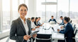 © Kaluya Stock - Asian businesswoman holding a tablet, smiling at the camera, with a team in the background