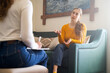 © Соня Монштейн - Young woman talking to psychologist during therapy session, sitting on sofa, female sharing problems while psychologist listening to her, mental health support, counseling in cozy modern interior