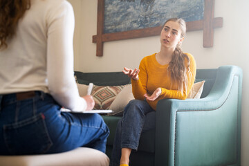 young woman talking to psychologist during therapy session, sitting on sofa, female sharing problems