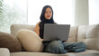 © wattana - Relaxed asian female remote worker using a laptop in a cozy living room.