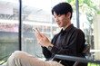 © wattana - Casual lifestyle moment of a man checking his phone in a relaxed, sunlit environment.