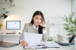 © wattana - Young businesswoman feeling stressed and overwhelmed while reviewing financial documents at her desk.